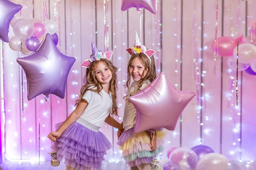 Two girls dressed up as unicorns posing in front of balloons.