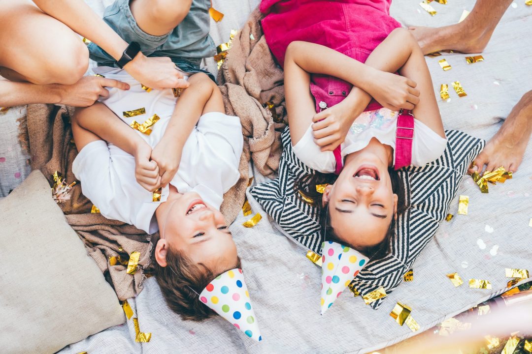 A group of children laying on the ground with party hats.