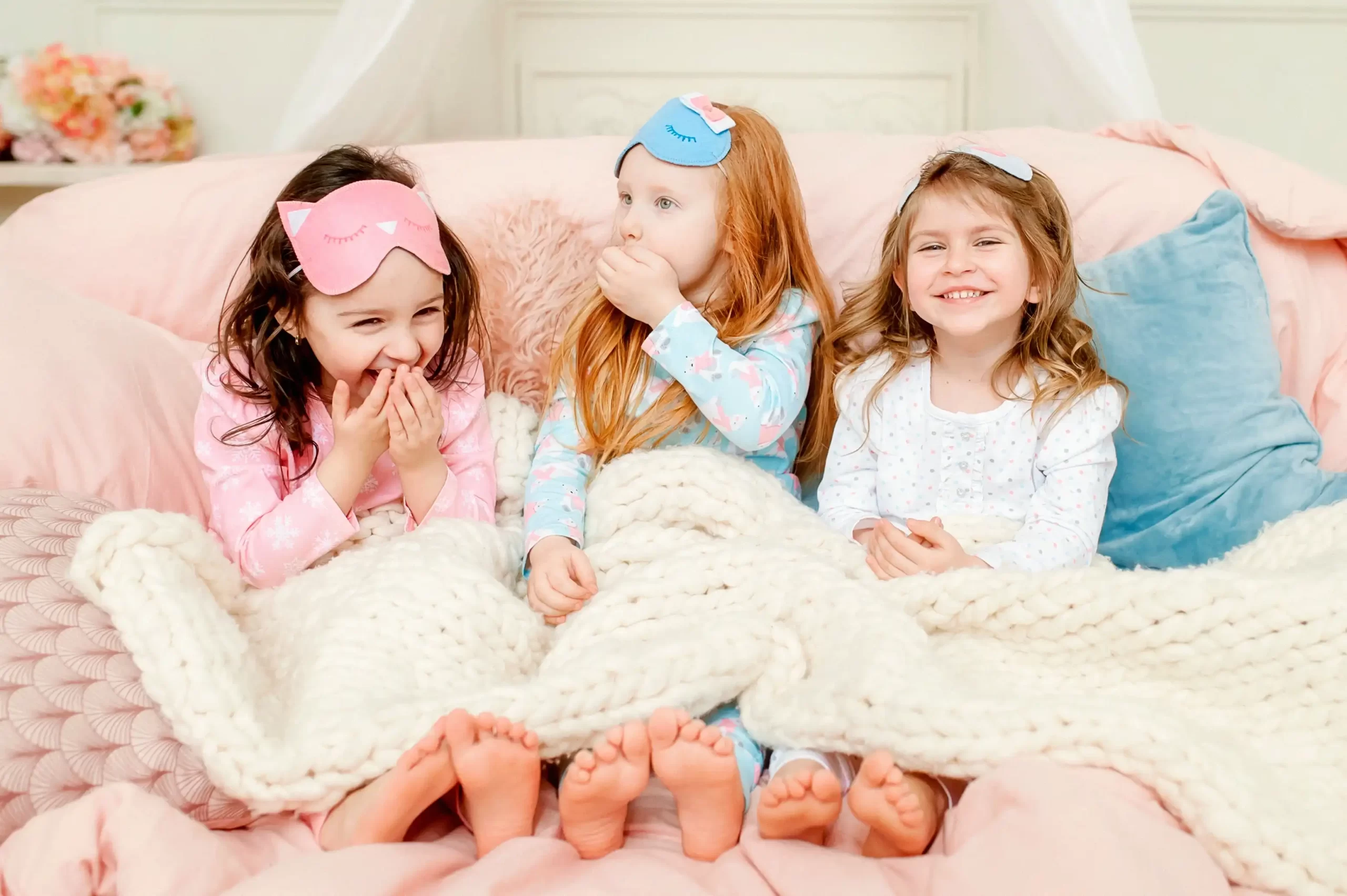 Three young girls enjoying an enchanting Teepee sleepover experience in cozy pajamas with sleep masks on their heads.